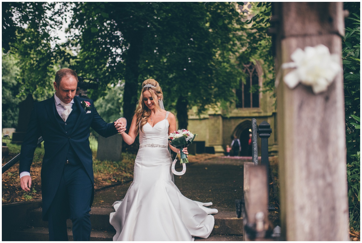 The groom leads his new wife away from the church towards their wedding car.