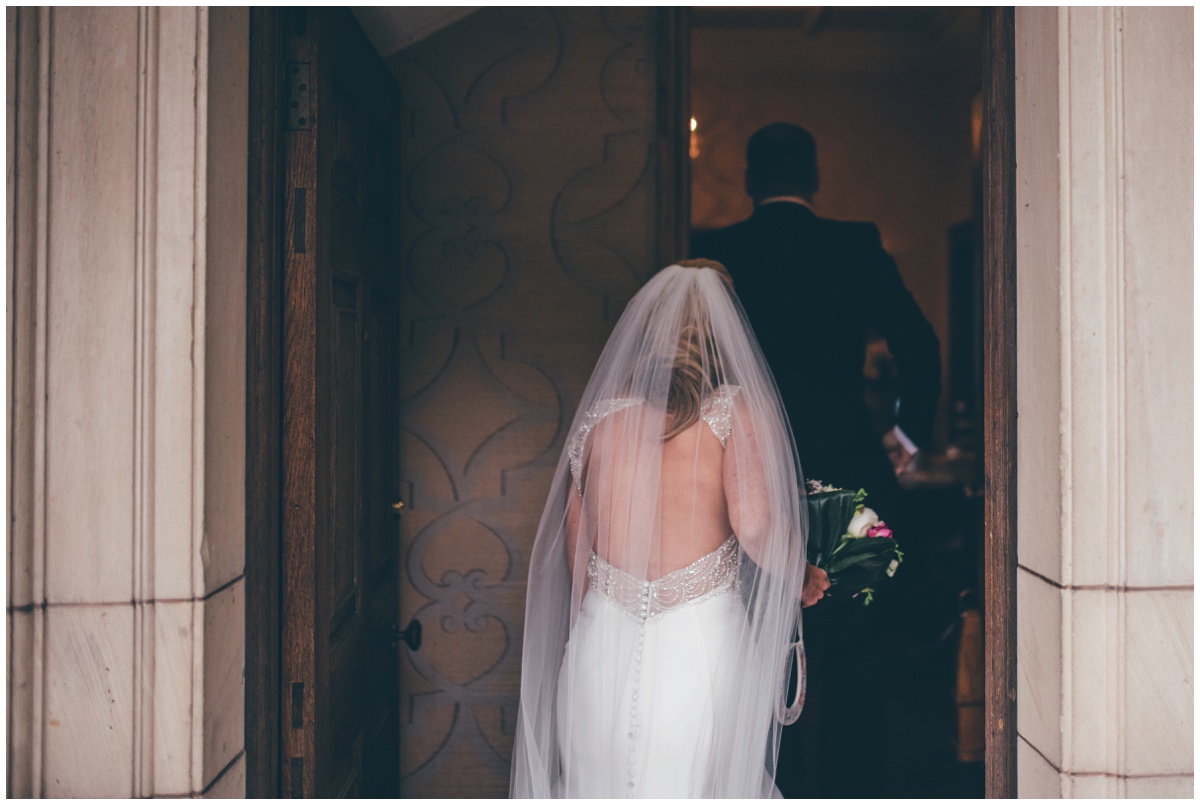 The beautiful detailed back of the bride's wedding dress shows as she walks nto her wedding venue, Willington Hall in Cheshire.