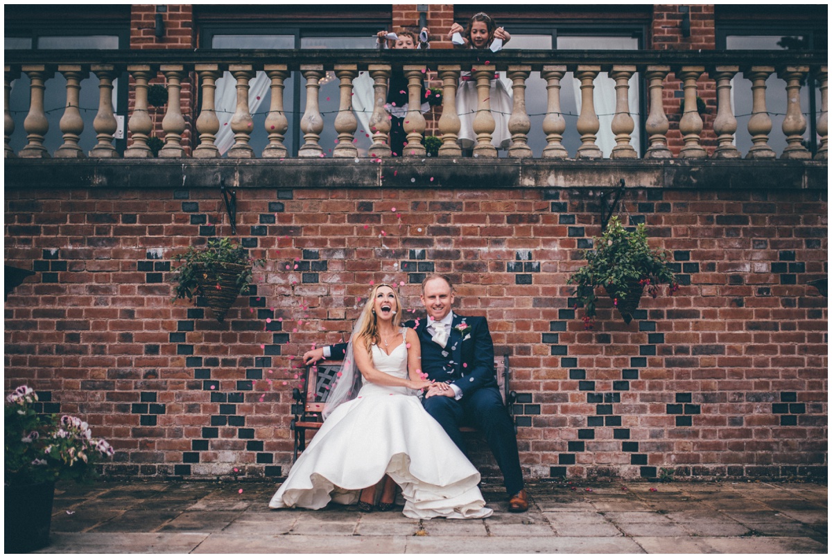 Cute moment of bride and groom being covered in confetti by cheeky flower girl and pageboy.