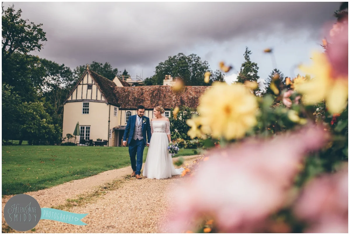 The bride and groom stroll through the pretty and flowery gardens at Bassmead Manor in Cambridgeshire.