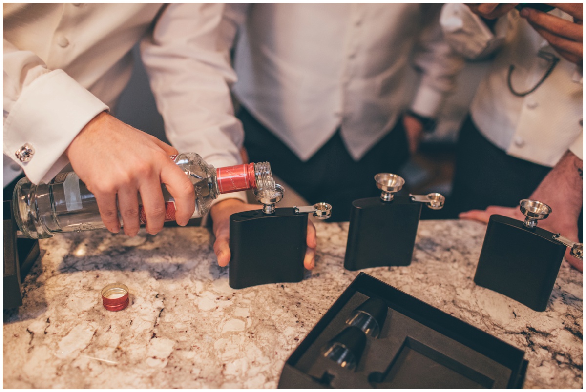 The groom pours vodka into hip flasks for himself and the boys.