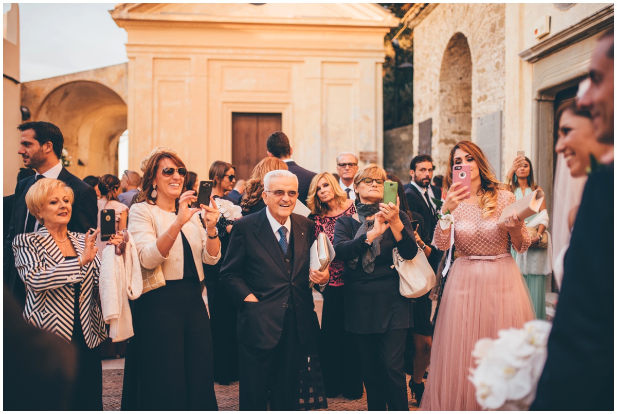 The youger guests take photographs of the new husband and wife on their phones, whilst the older guests just looks on happily.