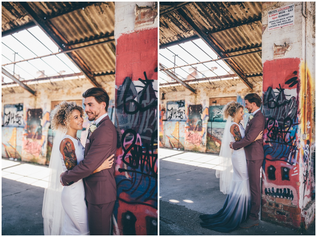 Beautiful newlyweds lean against graffiti covered wall posing for wedding photographs in Chester.