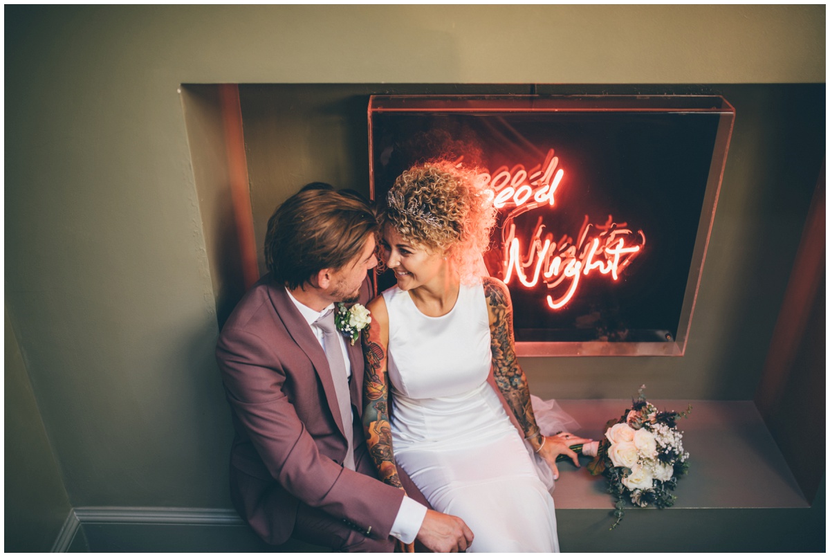 Bride and groom sit in front of bright neon lights in Oddfellows in Chester.