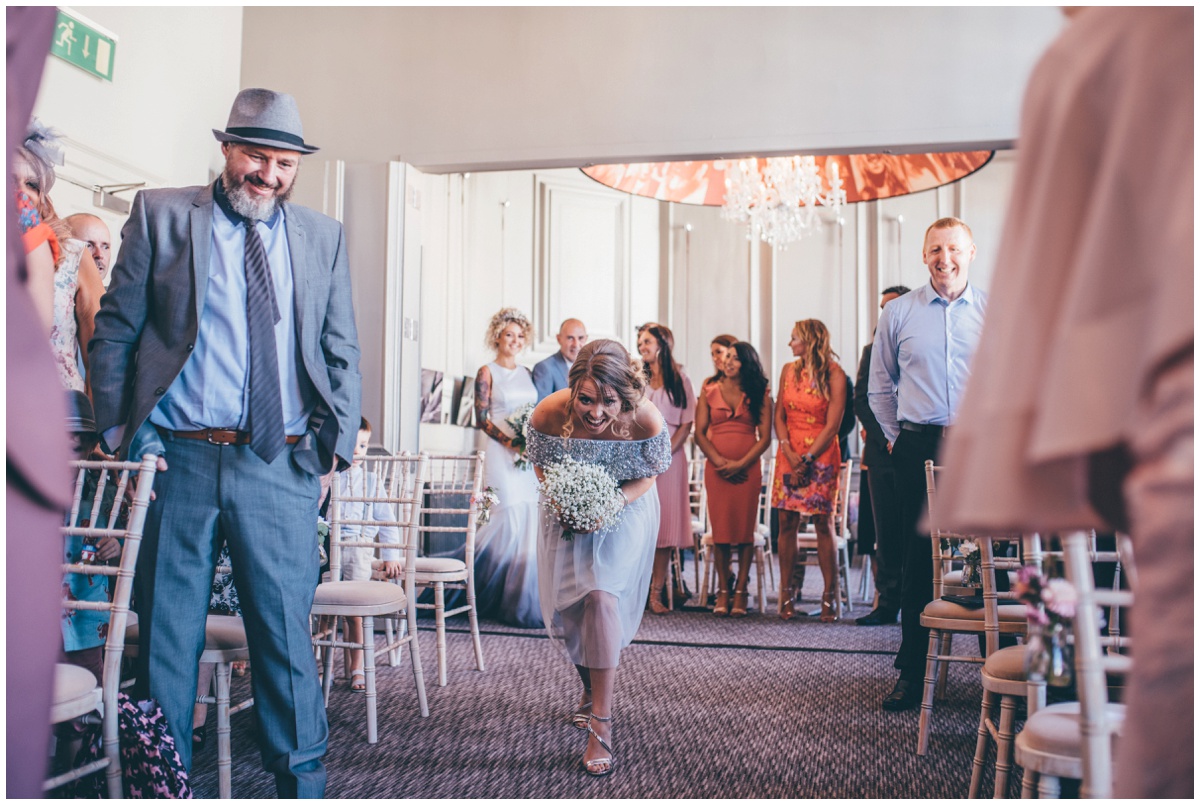 Bridesmaid smiles at flowergirl when she walks down the aisle in Oddfellows, Chester.