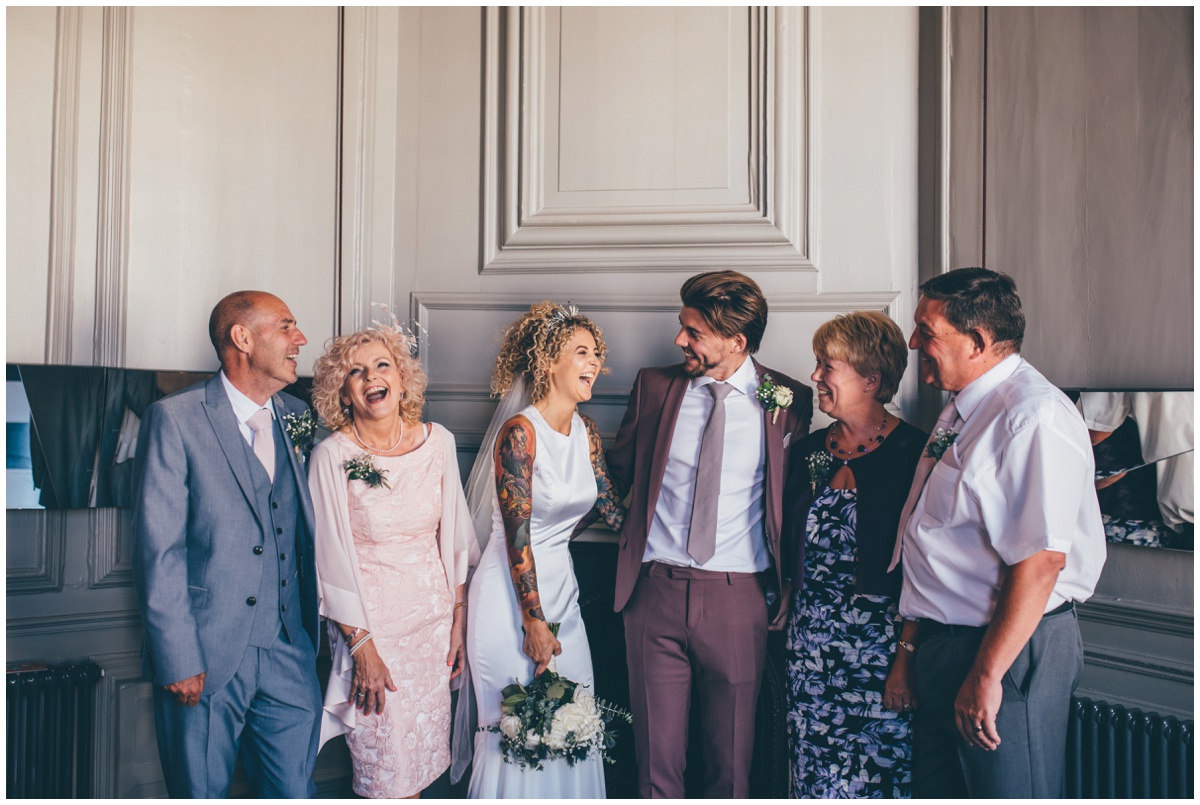 Tattooed Bride and her new husband in a pink suit laugh with their parents at Oddfellows in Chester.