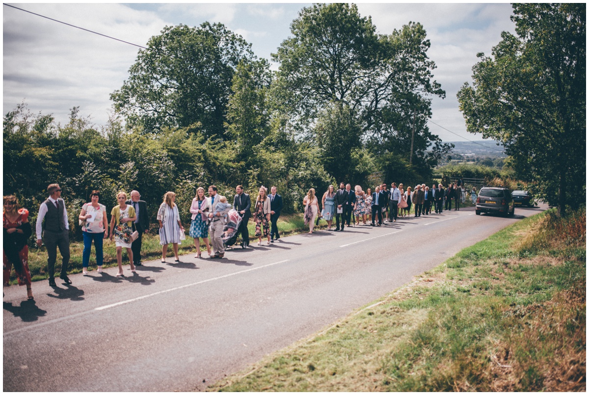 Wedding guests walk up the pretty country road, shot by Cheshire wedding photographer.