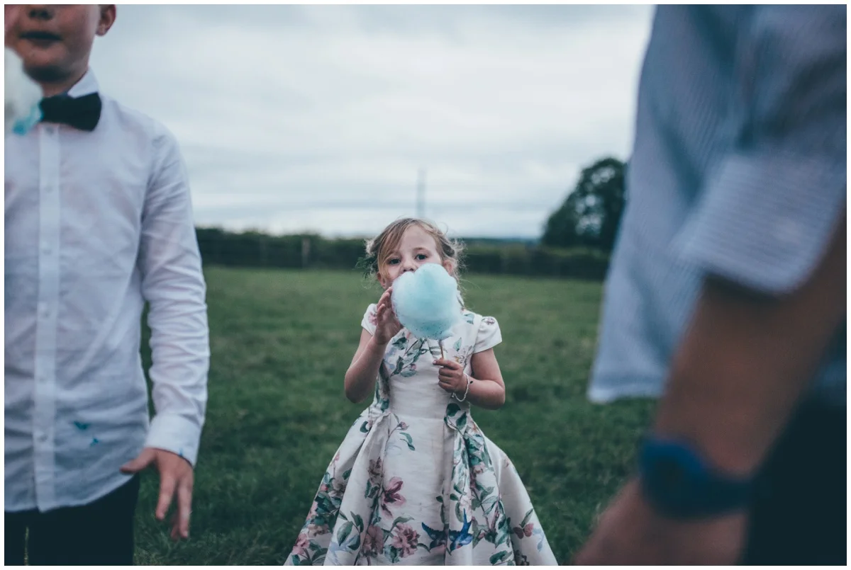 Cute flower girl enjoys candyfloss at a tipi wedding in Leek, Staffordshire.