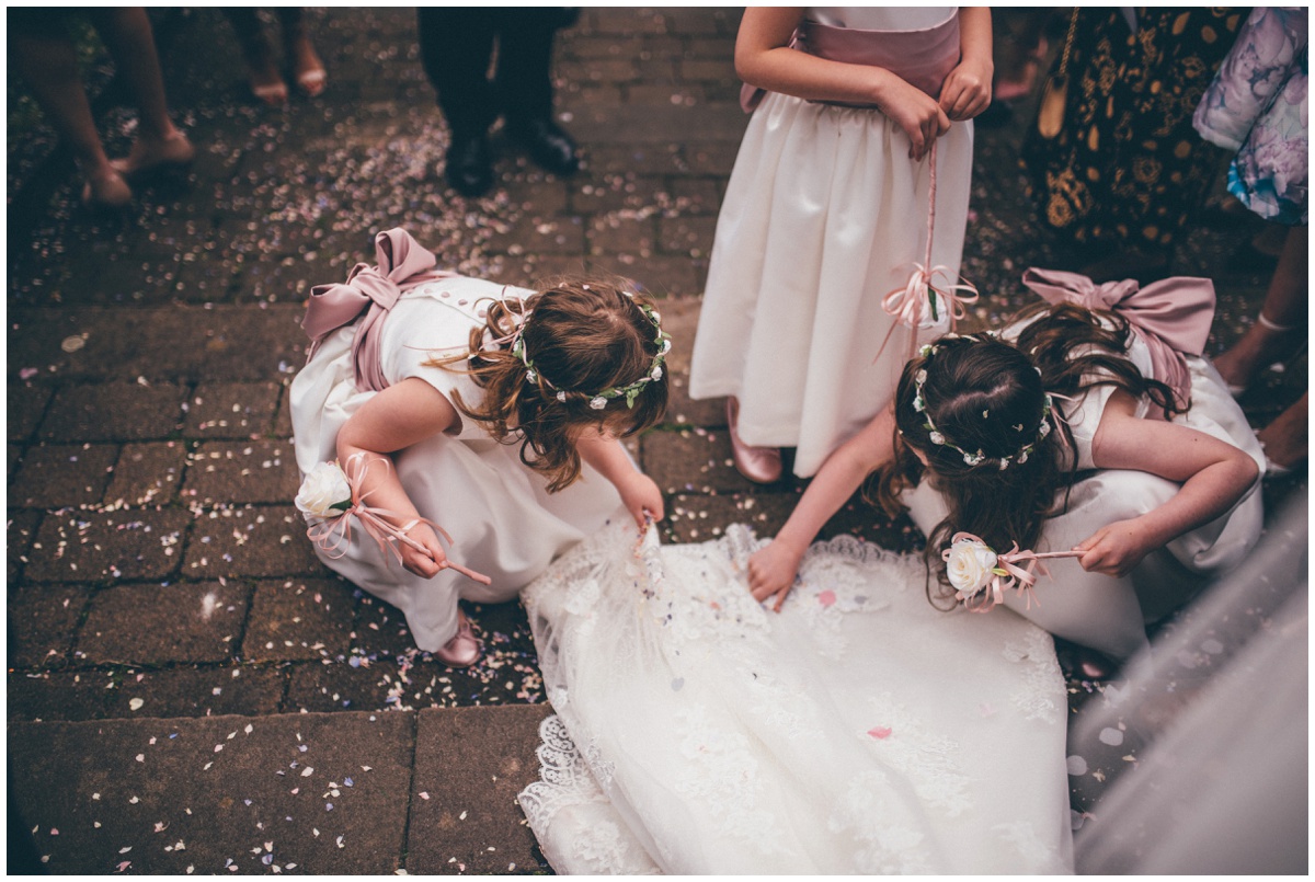 The flower girls pick confetti off the bride's beautiful lace train.
