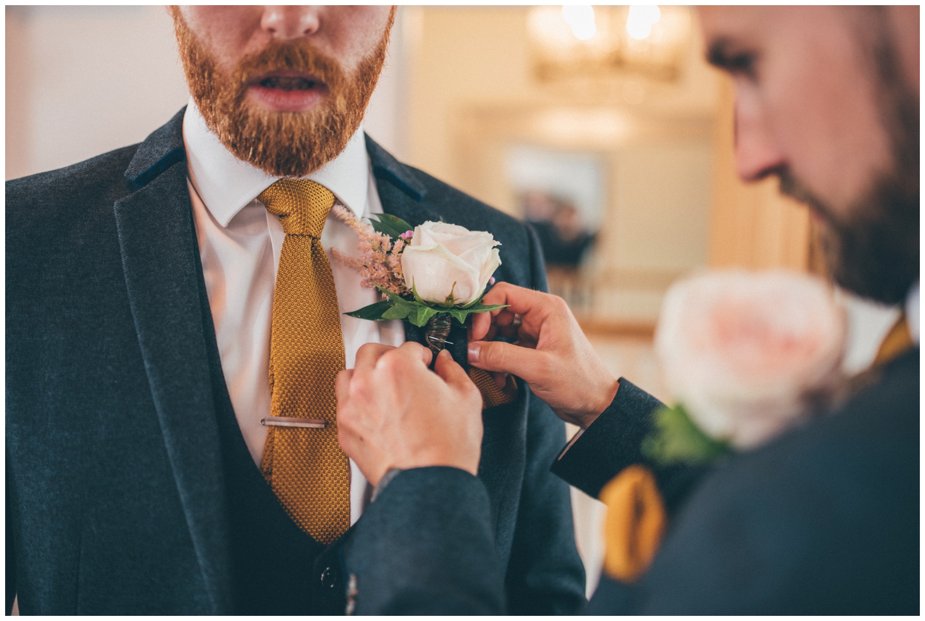 Groomsman fastens on the groom's button hole before the wedding at Tyn Dwr Hall in Wales.