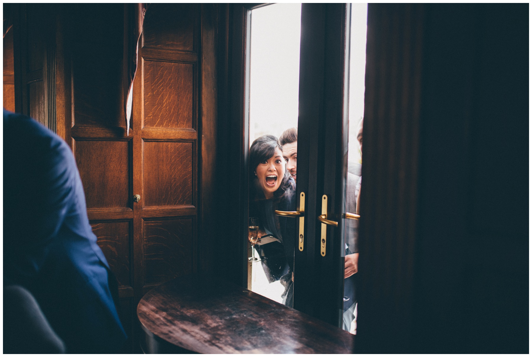 Family members make wedding guests laugh through the window at Langdale Chase hotel in the Lake District.