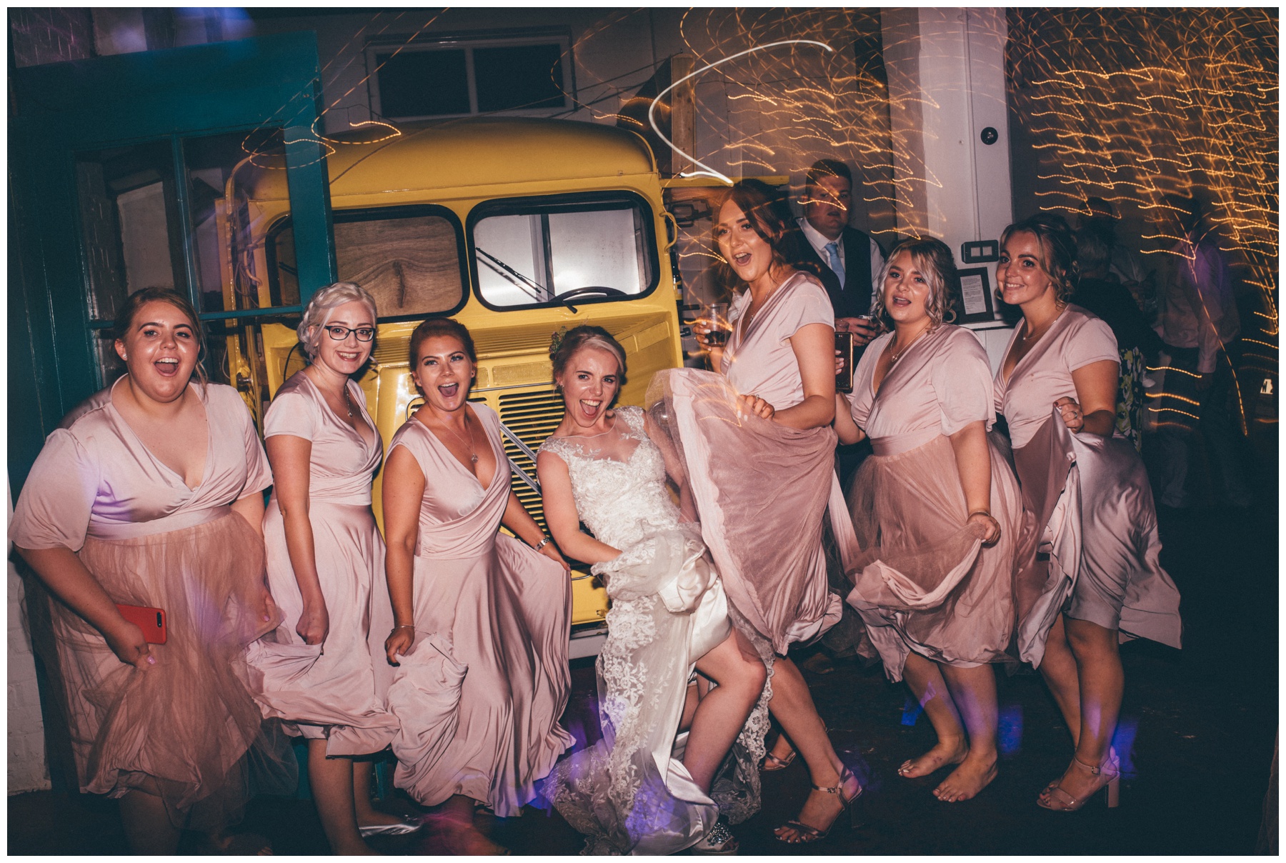 Bride and her bridesmaids all dance in their dusky pink dresses, in front of the for truck at The Hide wedding in Sheffield.