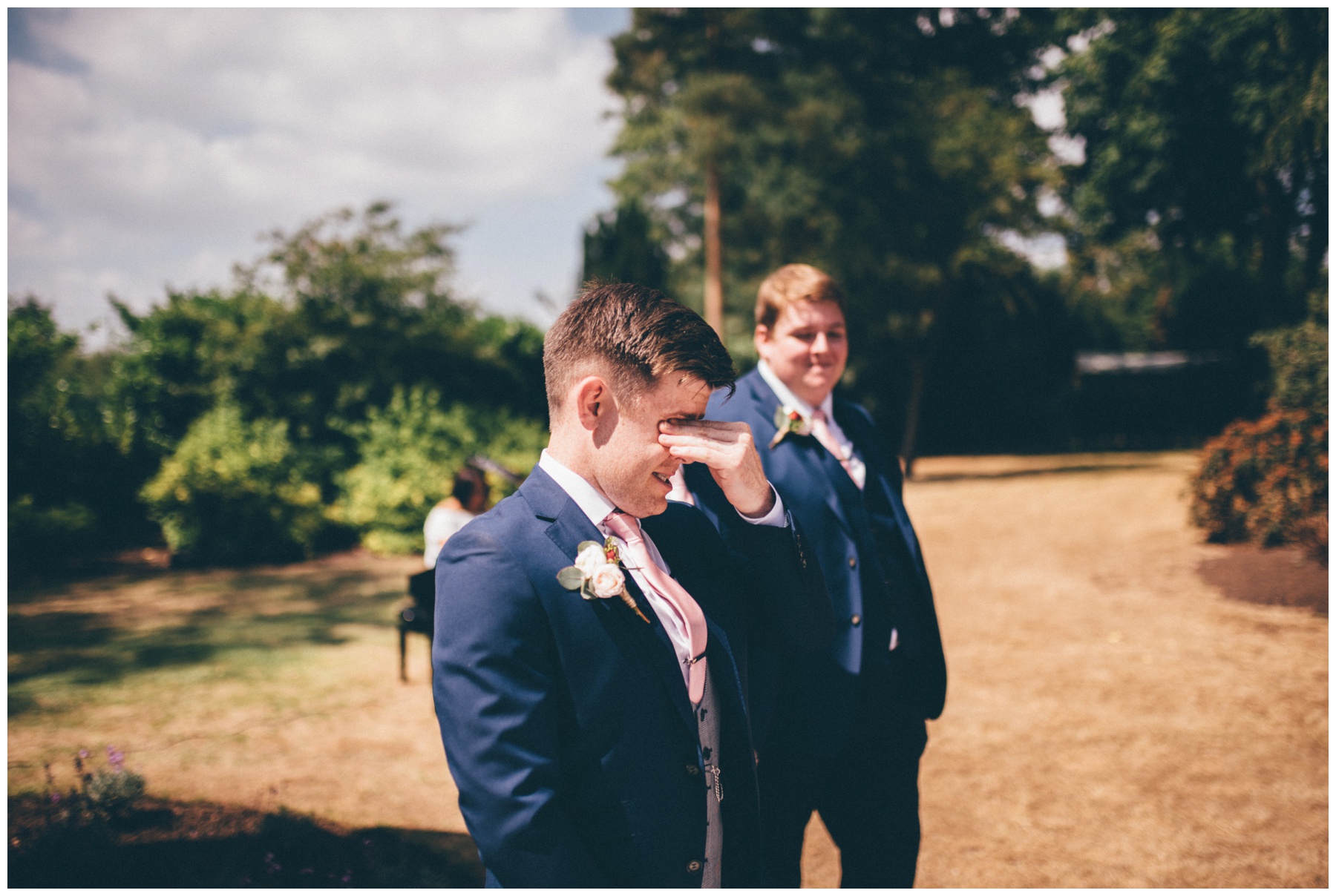 Groom cries as he watches his bride walk down the aisle at their outdoor wedding ceremony at Tilstone House in Cheshire.