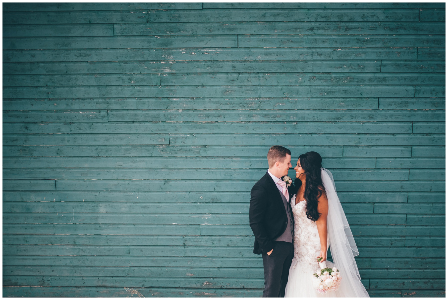 Bride and groom stand against a green wooden backdrop at Aigburth cricket club wedding in Liverpool.