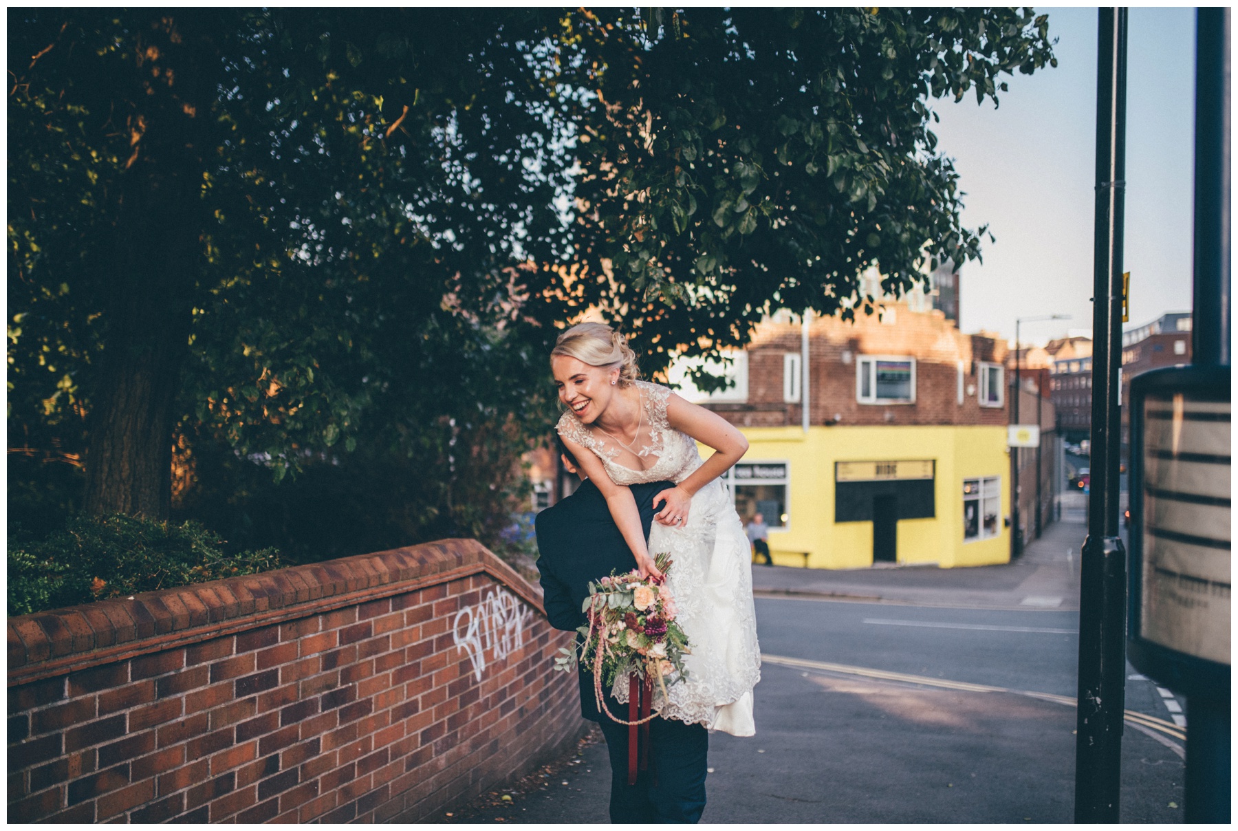 Groom gives his bride a fireman lift towards their Sheffield city centre wedding venue, The Hide.