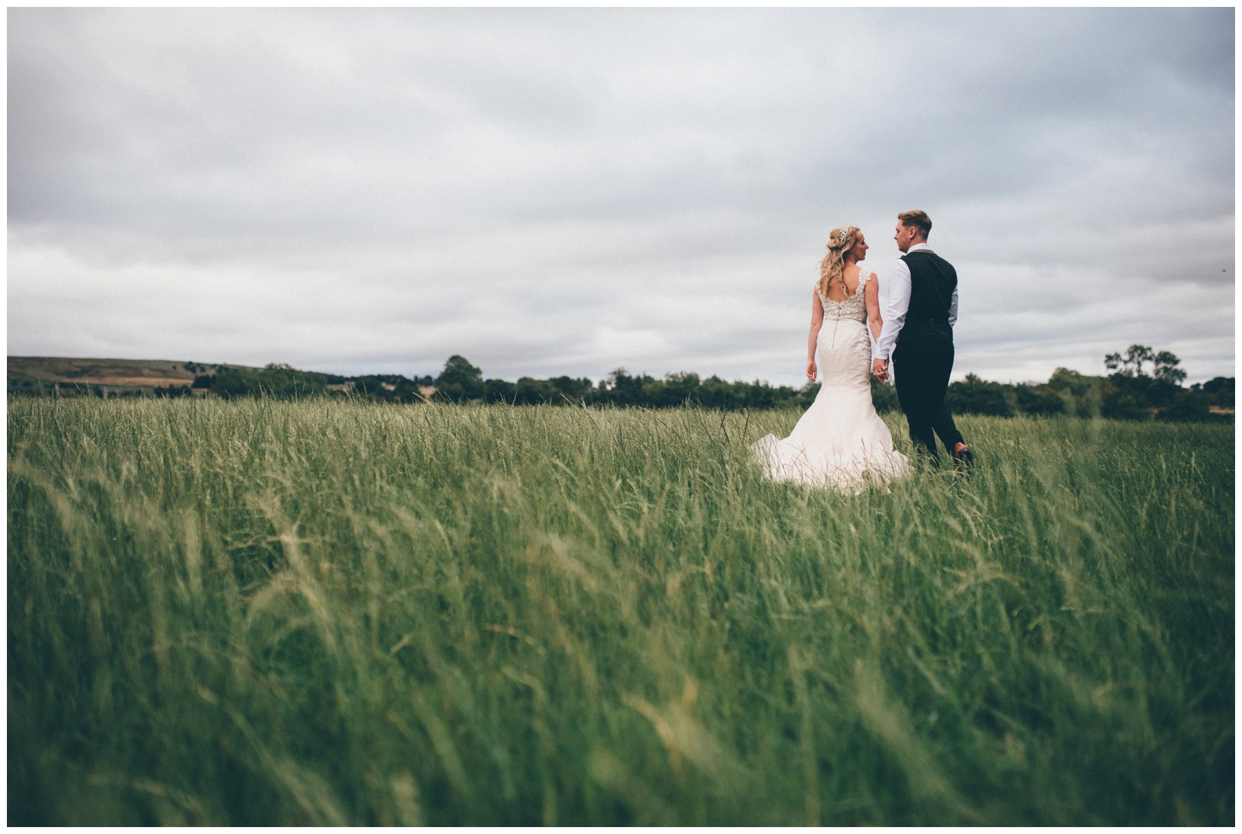 Staffordshire bride and groom walk through a field together on their wedding day near their tipi.