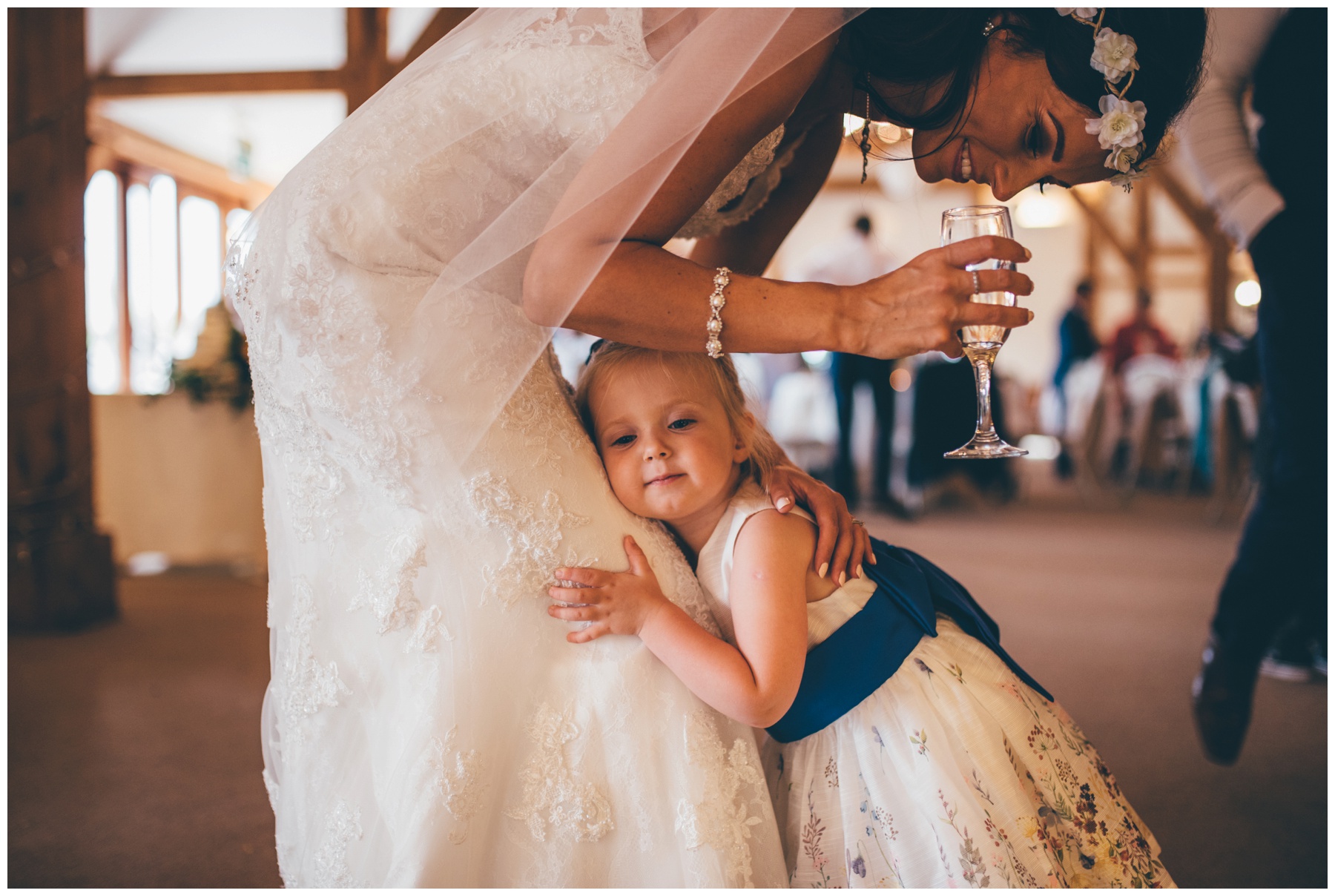 Cute little flower girl cuddles the bride at Sandhole Oak Barn in Cheshire,