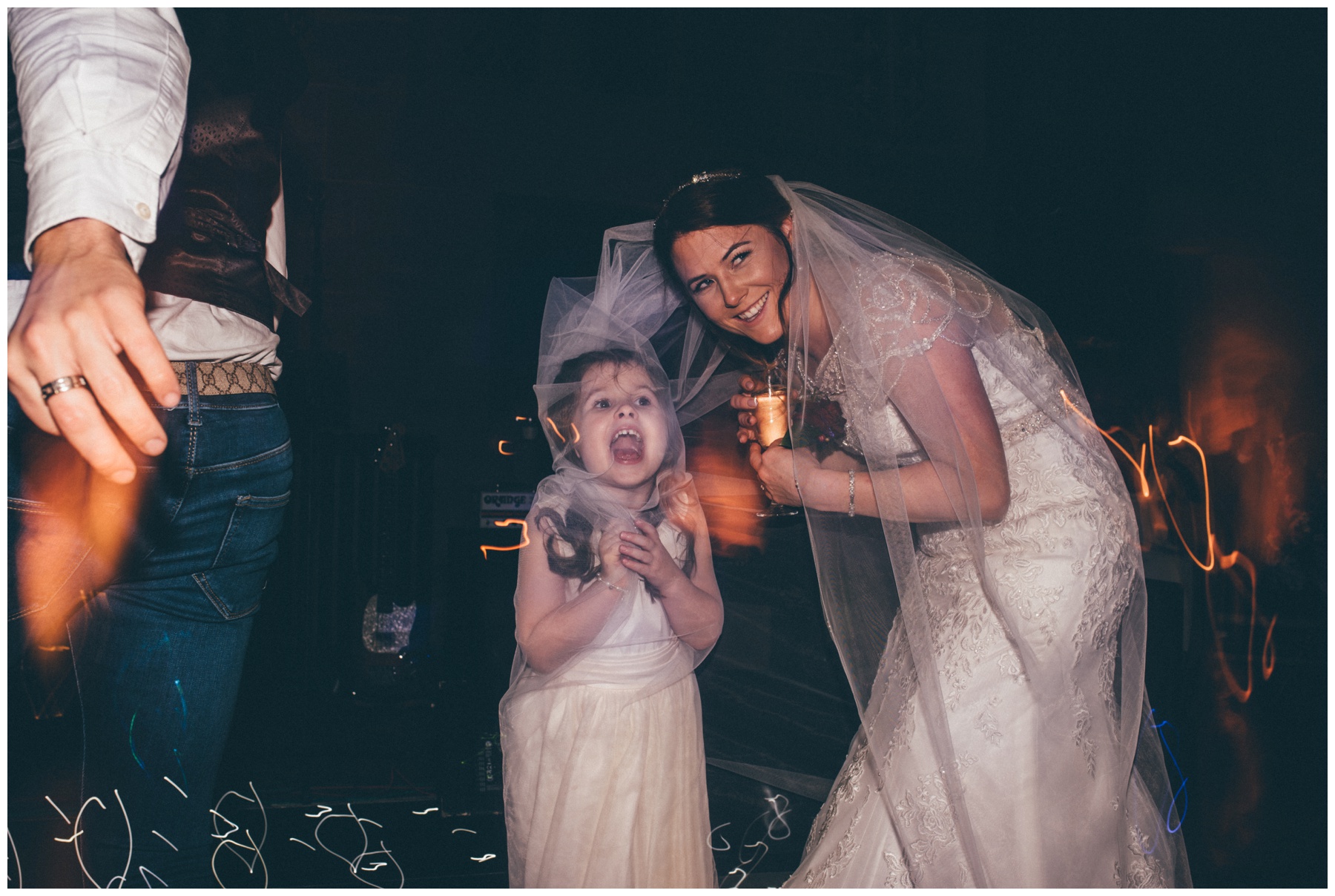 Cute flower girl and the bride both hide under the veil at Peckforton Castle in Cheshire.