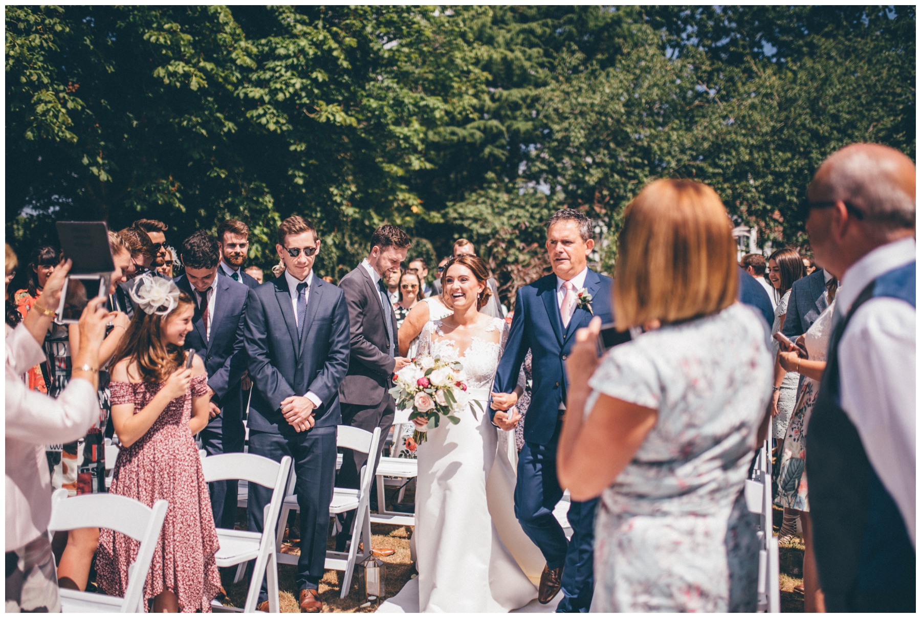 Bride walks down the aisle with her Dad at her outdoor wedding ceremony at Tilstone House.