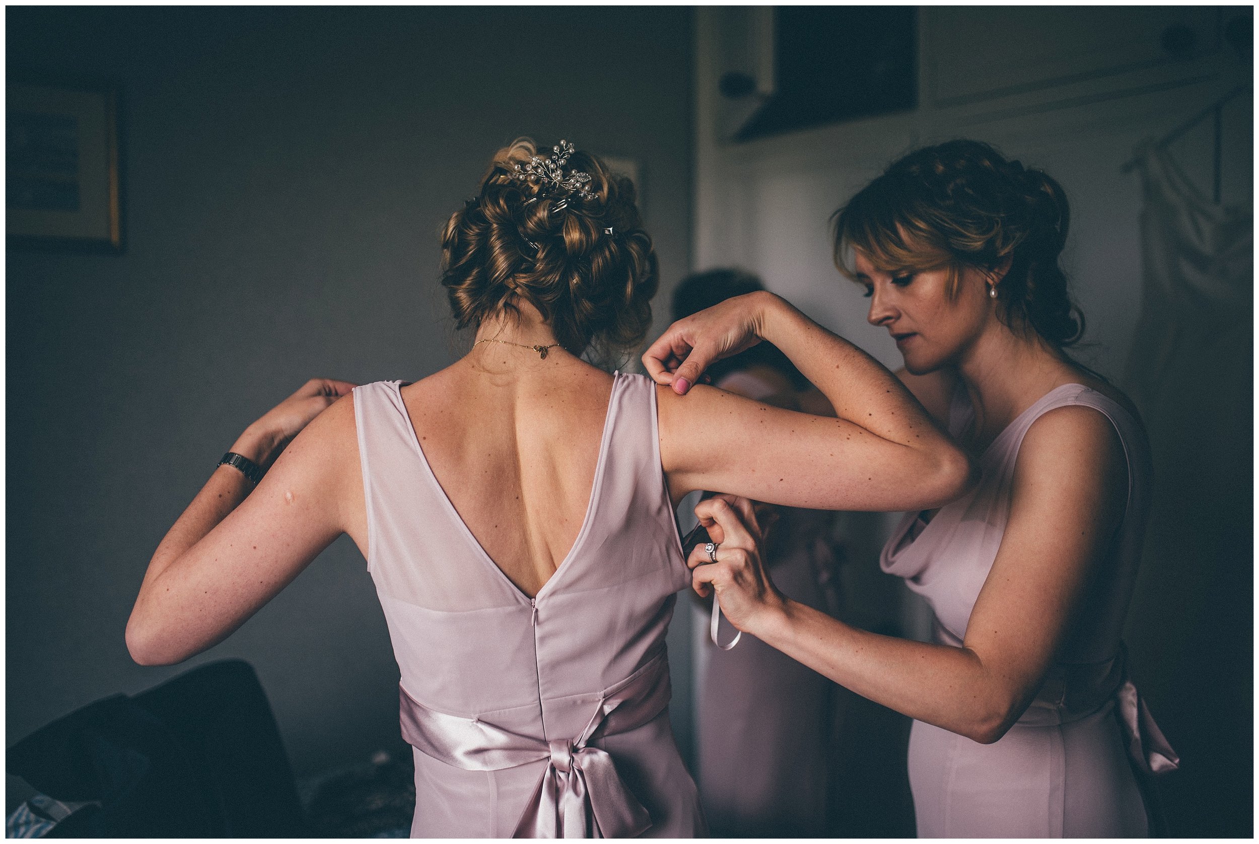 bridesmaids help each other into their dresses.