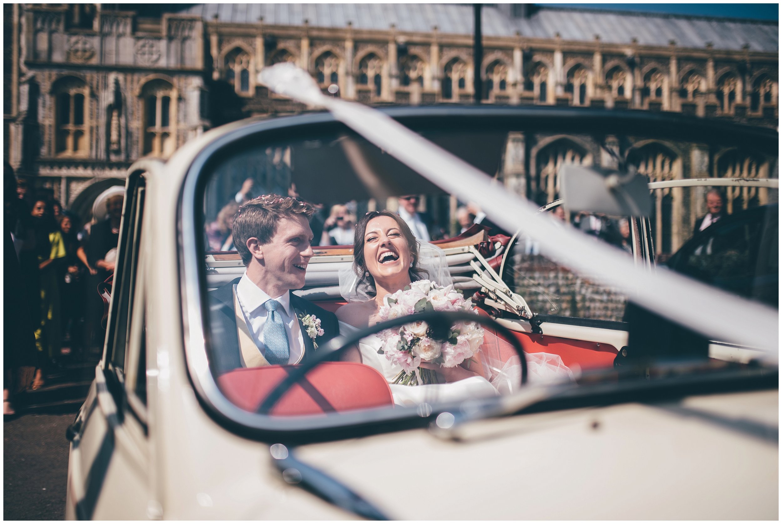 Bride and groom leave their wedding in their old classic car for their wedding reception.