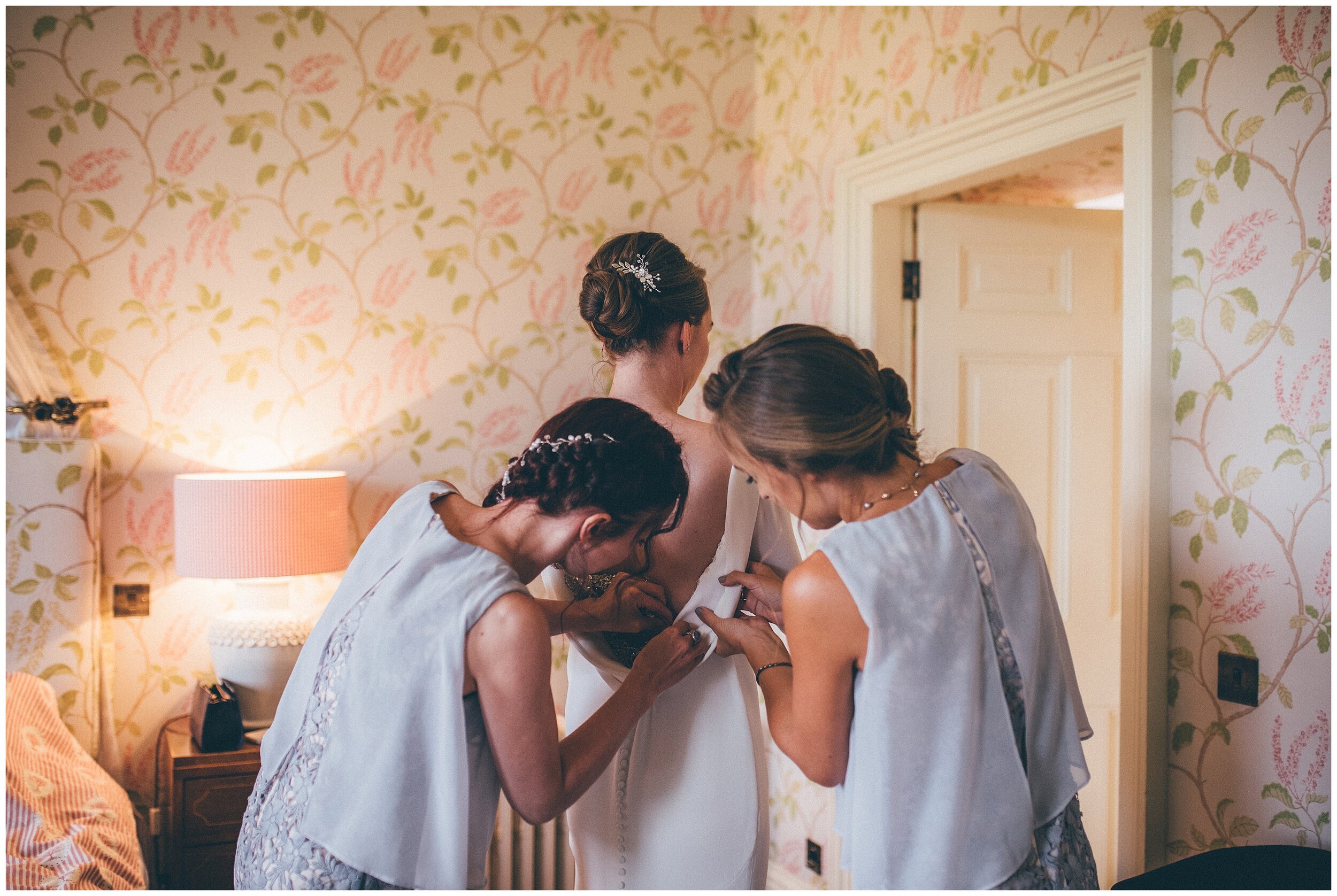 Bridesmaids wearing grey bridesmaid dresses help the bride into her Pronovias gown.