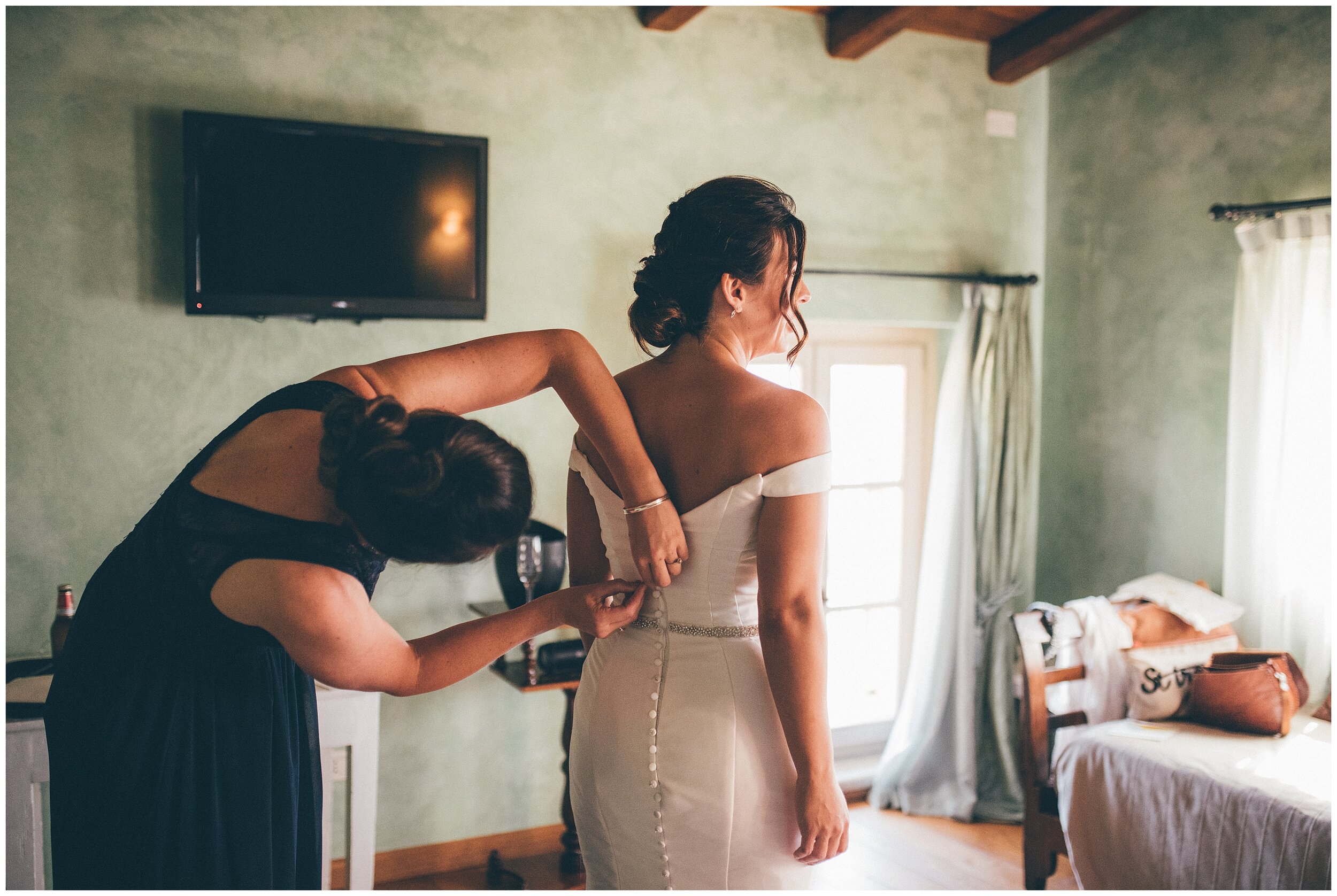 Bridesmaid helps bride into her beautiful Essence of Australia dress at Agriturismo Villa Bissiniga.