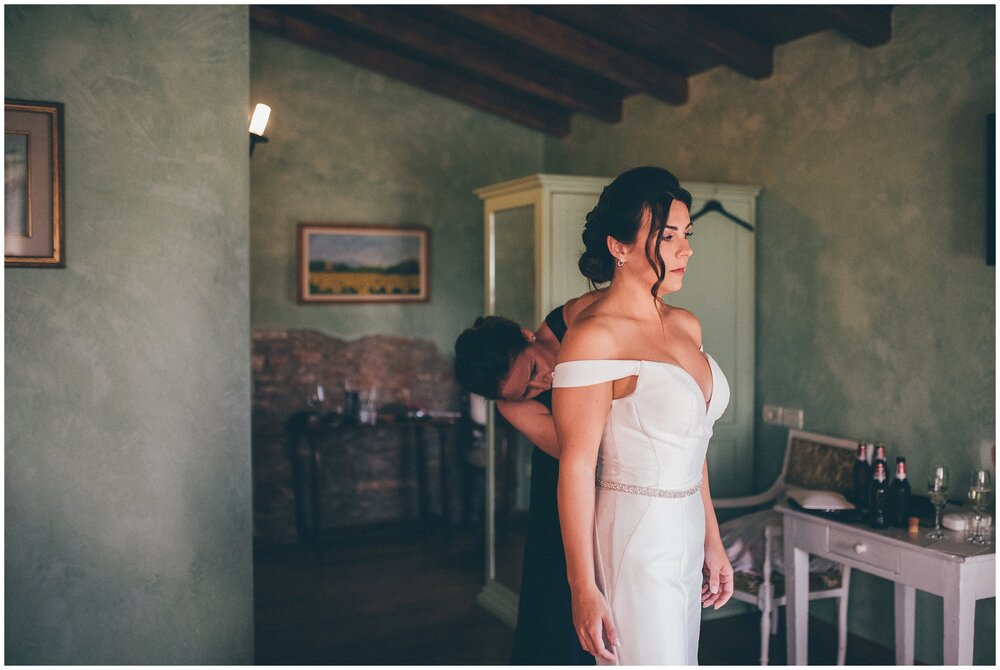 Bridesmaid helps bride into her Essence of Australia dress at Agriturismo Villa Bissiniga.