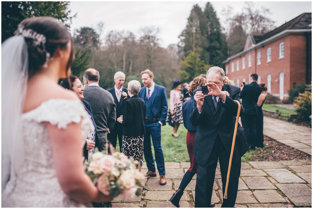 Bride's grandad takes a photograph of her at her wedding at Mottram Hall in Wilsmslow.