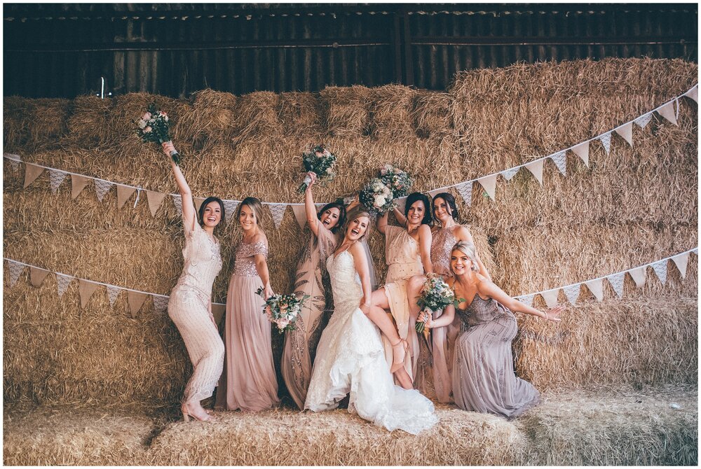 Bride and her bridesmaids pose on hay bails at Owen House Wedding Barn in Cheshire.