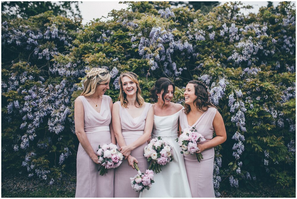 Suffolk bride with her bridesmaids in front of beautiful wisteria at Henham Wedding Barns.