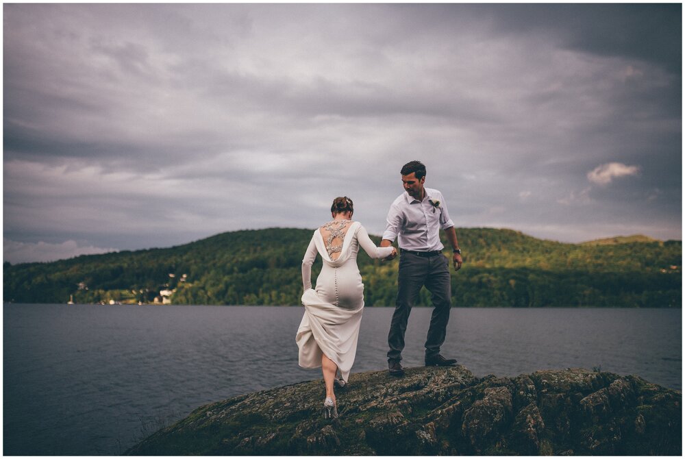 Groom helps his new wife up Grubbins Point rock for their wedding photographs in the Lake District.