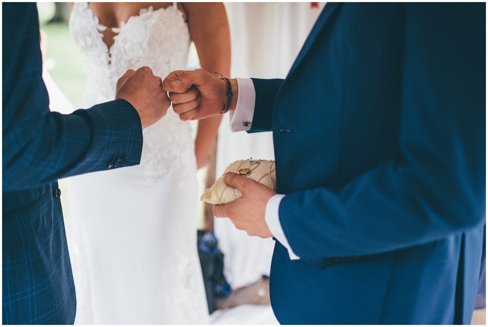 Groom and Best Man fist bump whilst he hands over the wedding rings at Chippenham Park Gardens.