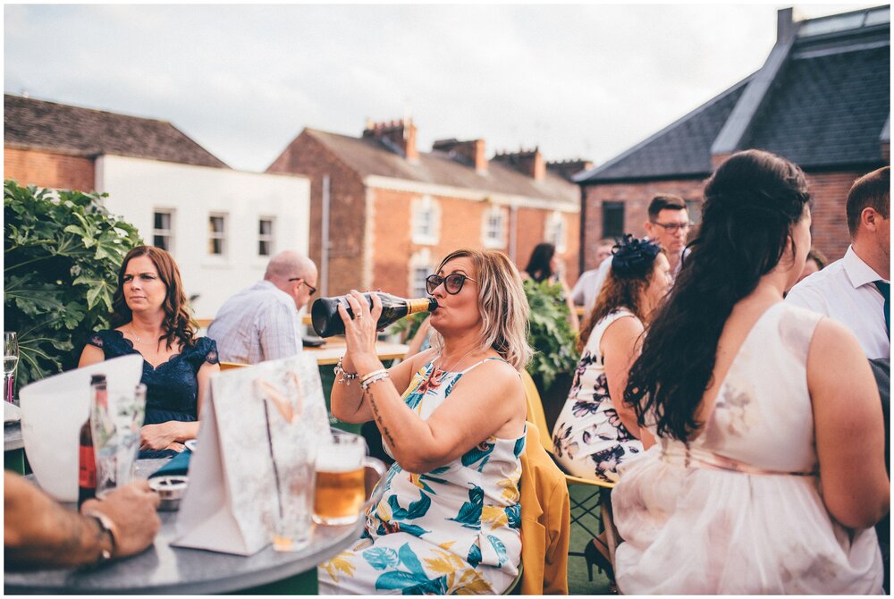 Wedding guest drinks from bottle of prosecco at summer wedding in Chester at Oddfellows.