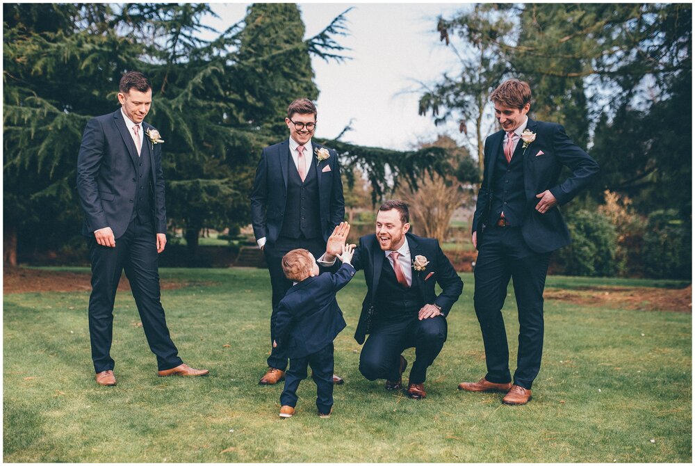 Cute page boy high fives the groom and his groomsmen at Mottram Hall wedding.