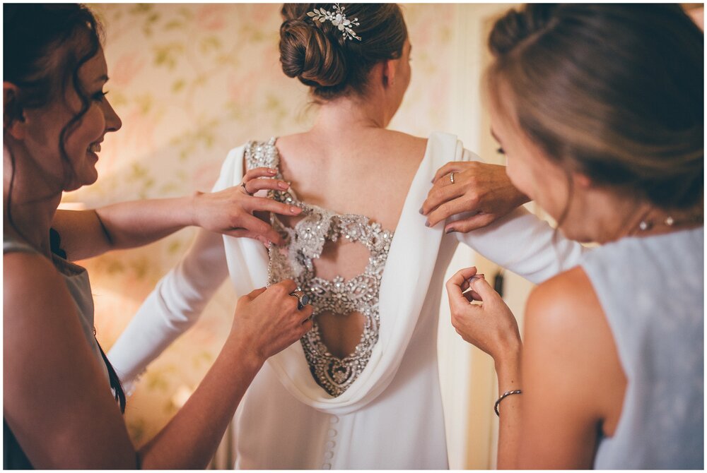 Bridesmaids help the bride into her wedding gown.