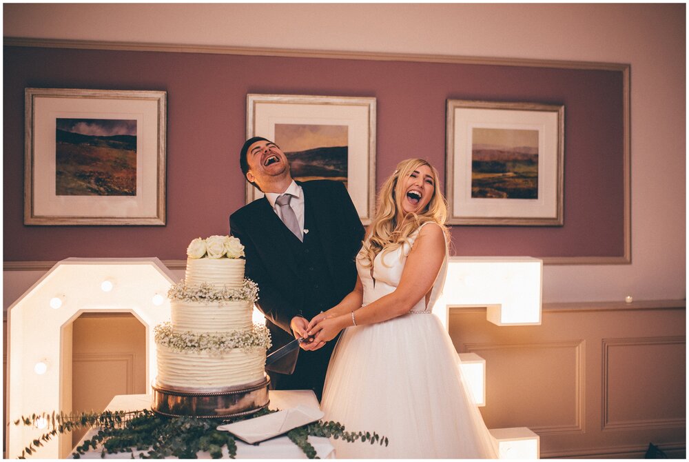 Bride and groom laugh with each other as they cut their cake at The Belsfield in the Lake District.