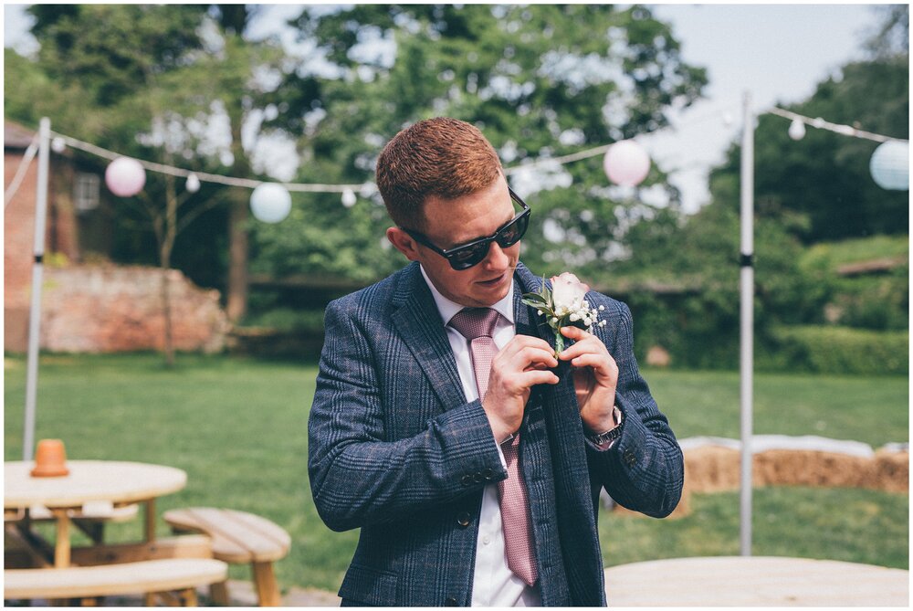 Groom puts on his buttonhole before his rustic wedding in Cheshire.