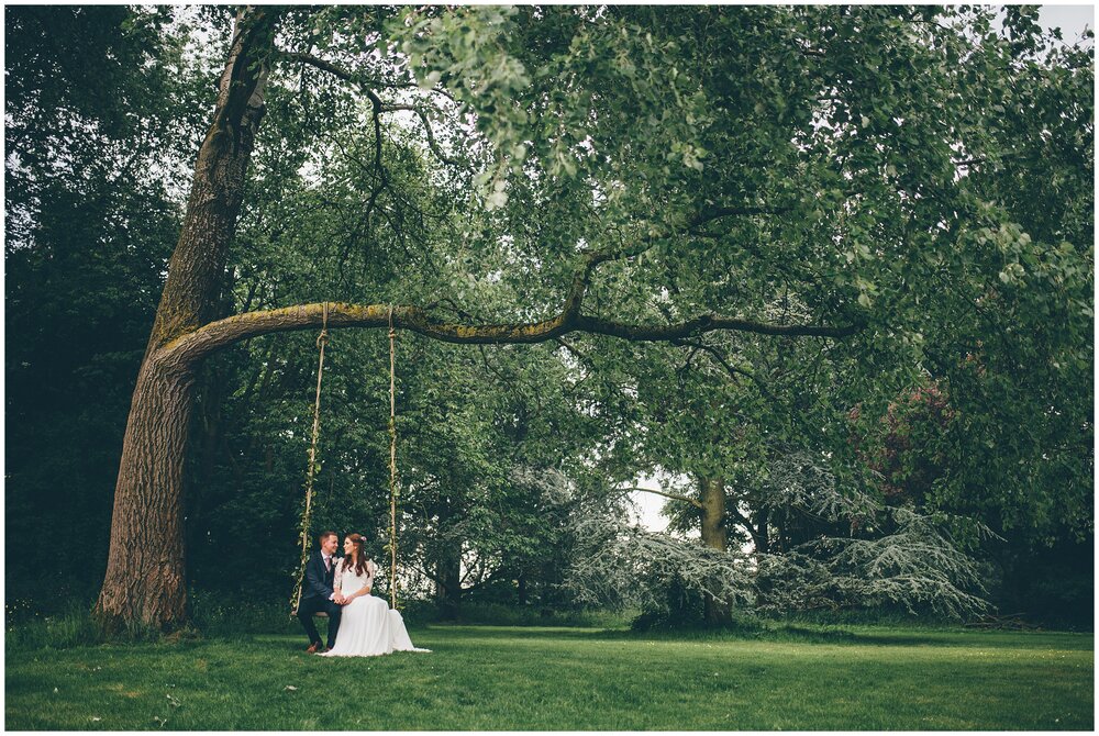 New husband and wife sit on a huge tree swing together.