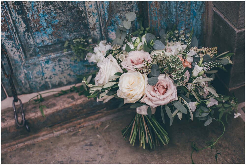 Incredible pastel bridal bouquet in front of a blue rustic door by florist Issy and Bella in Hereford.