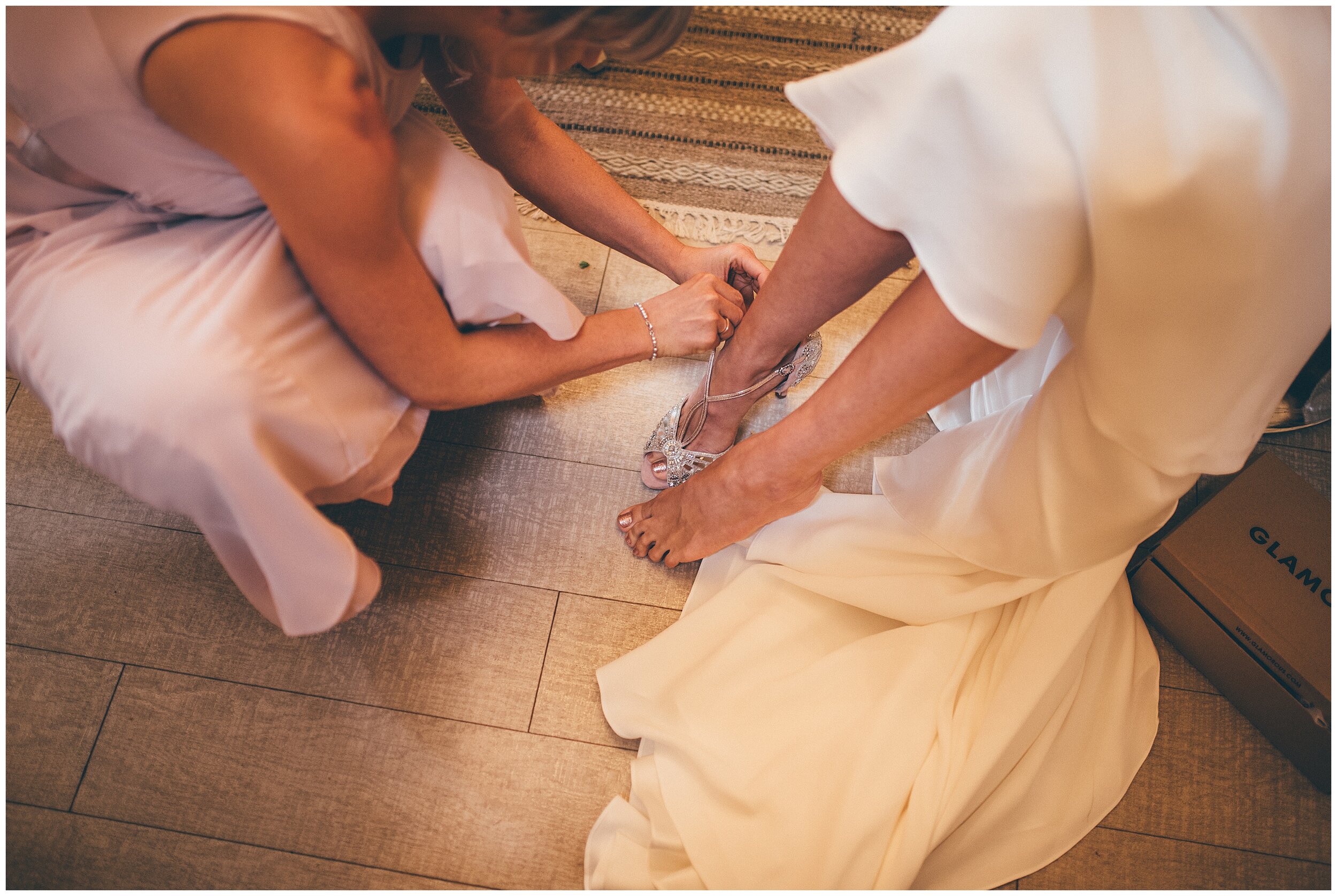 A bridesmaid fastens the bride into her pink and mirrored Emmy shoes.