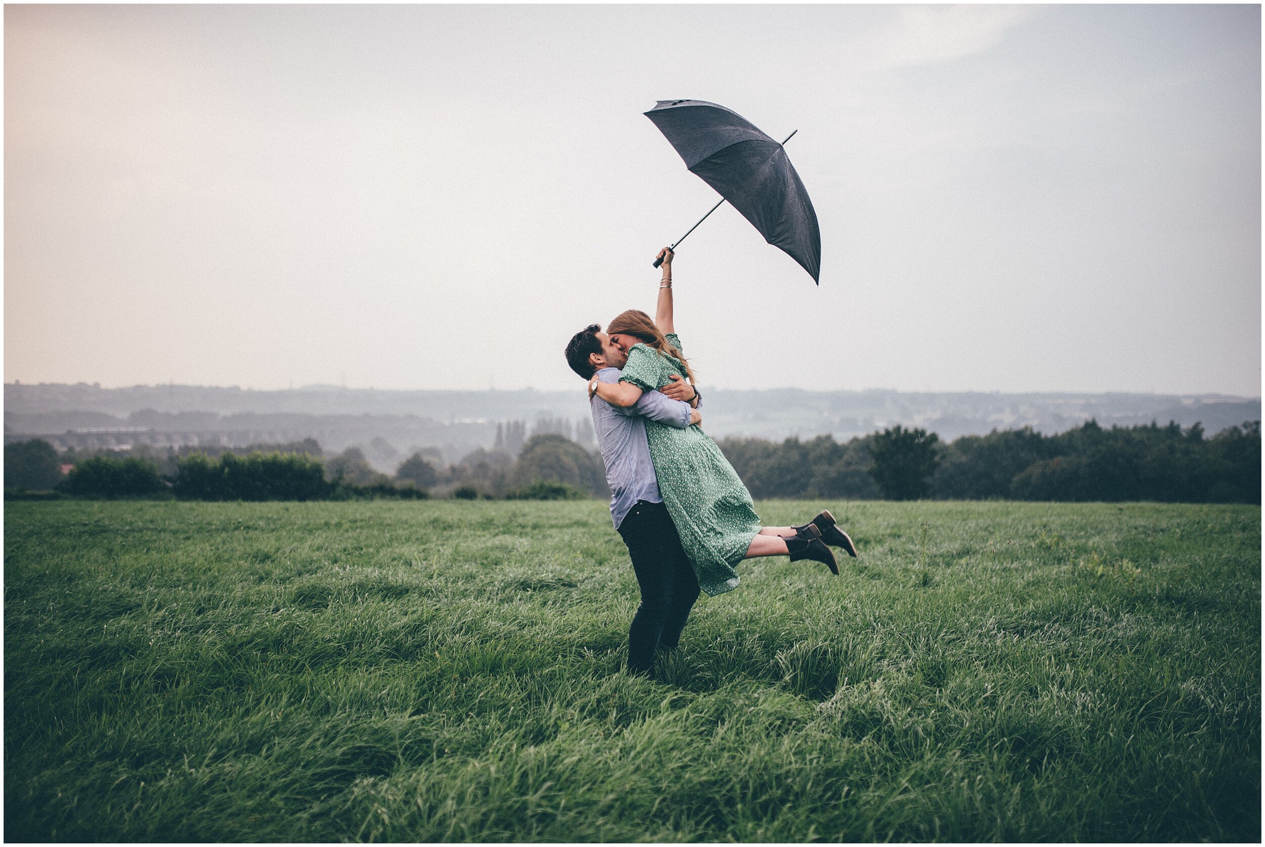 Couple with black umbrella as boyfriend lifts up his girlfriend.