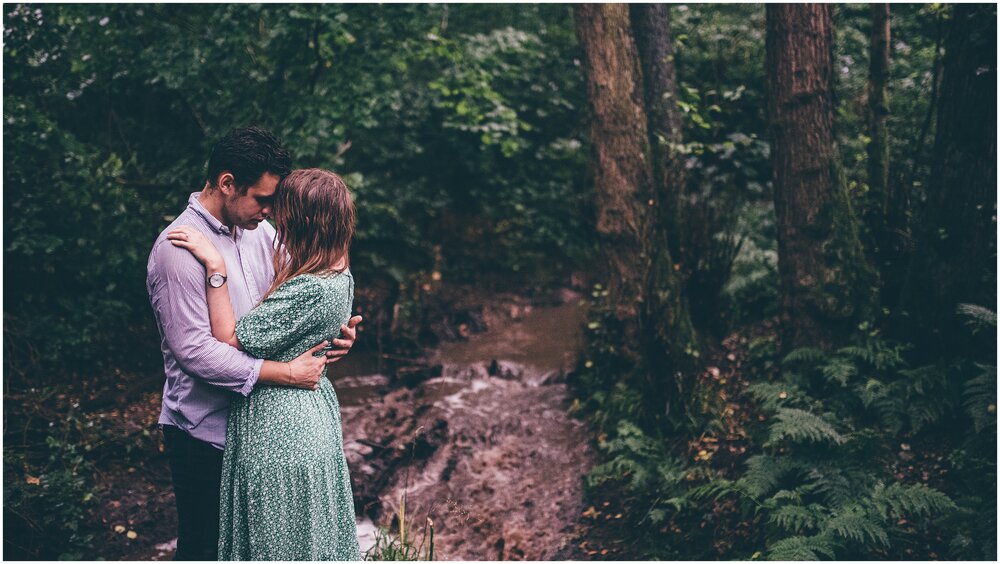 Couple pose together next to a woodland stream in the rain in Cheshire.