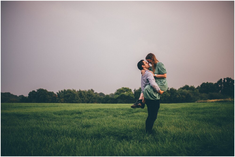 Man holds up his fiancé in embrace in a field in a thunderstorm in Cheshire.