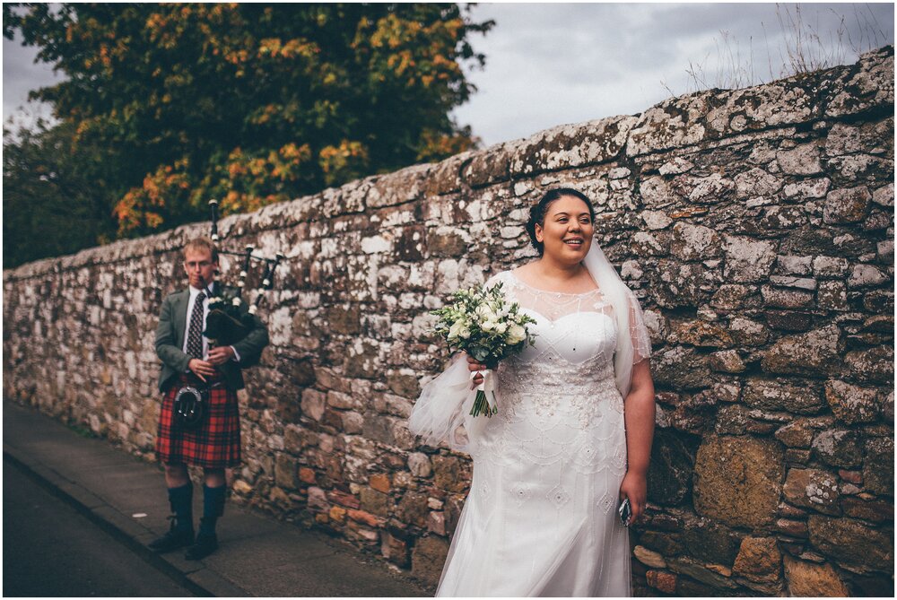 Bride waits for her groom with bagpipe player in the background.
