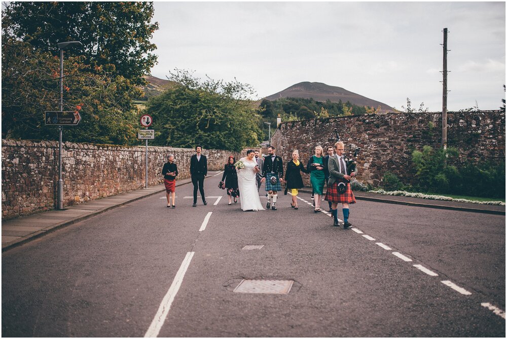 Bride and groom walk after their wedding through Melrose following a bagpipe player.