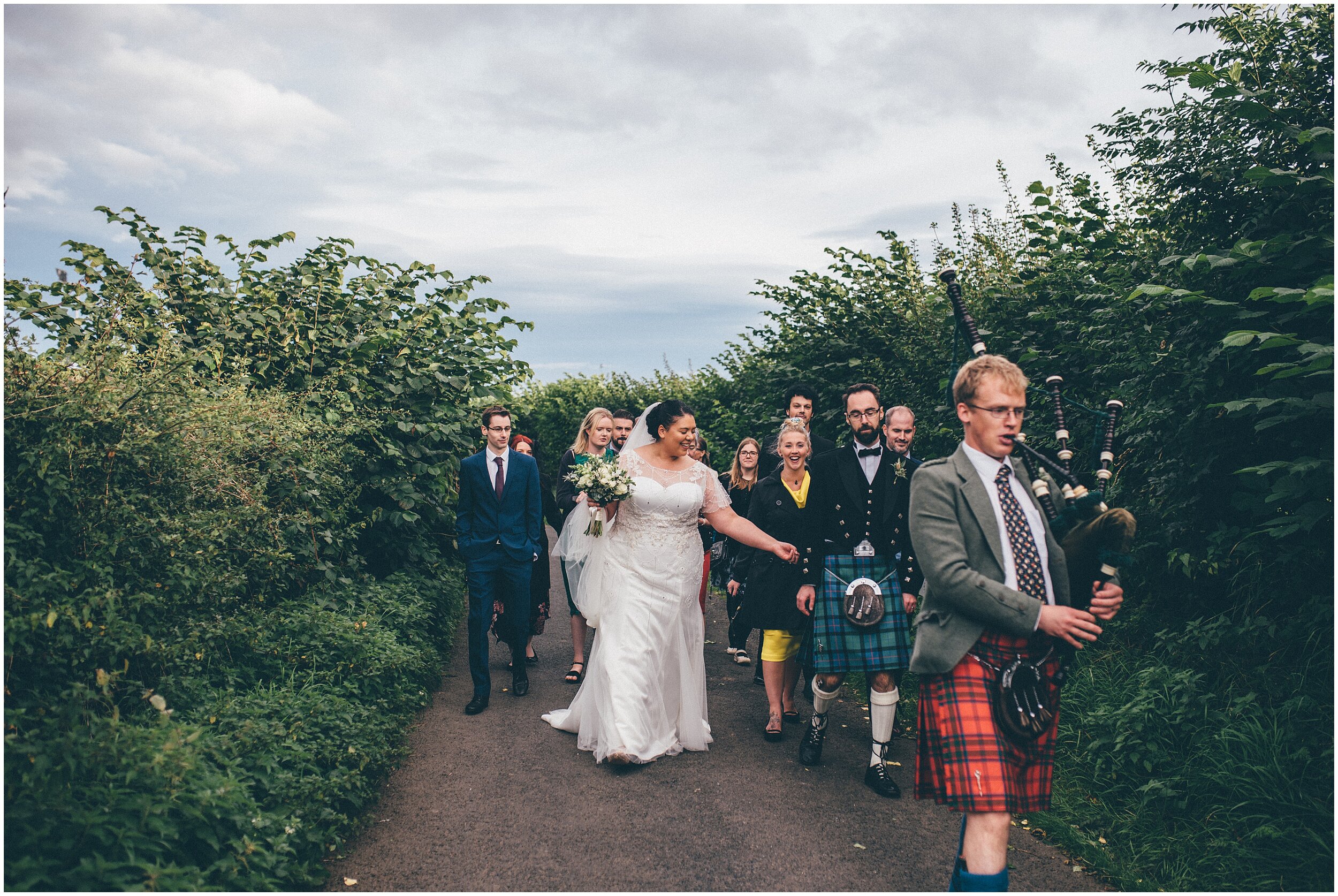 Bride and groom walk after their wedding through Melrose following a bagpipe player.