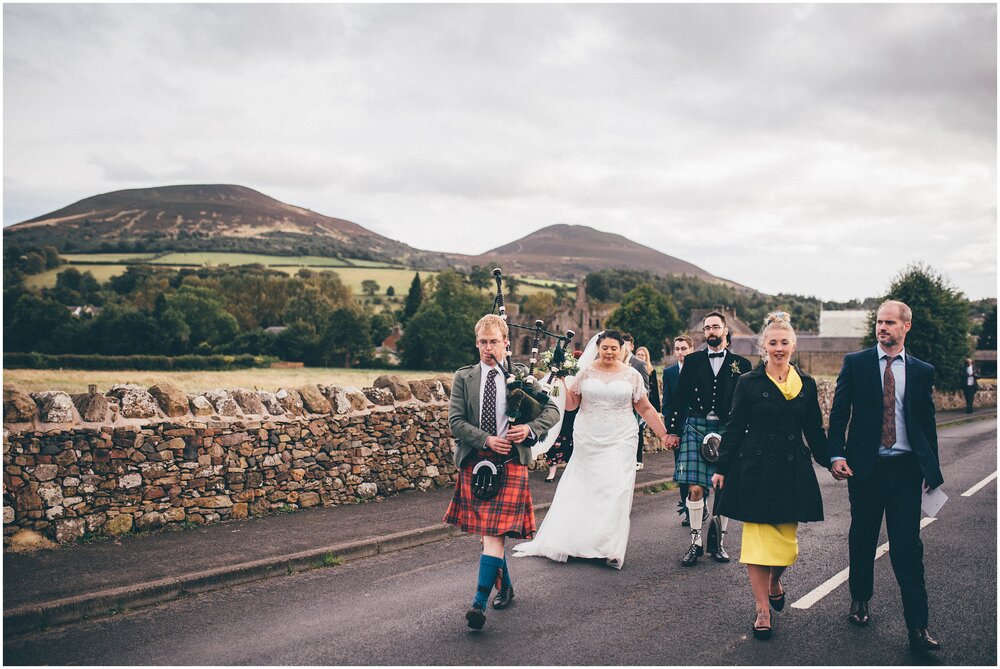 Bride and groom walk after their wedding through Melrose following a bagpipe player.