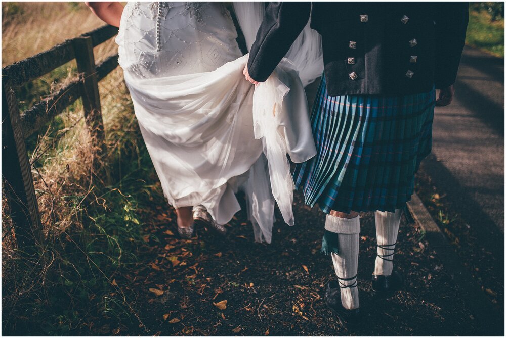 Groom helps his new wife with her dress on the walk to their wedding reception in Melrose, Scotland.