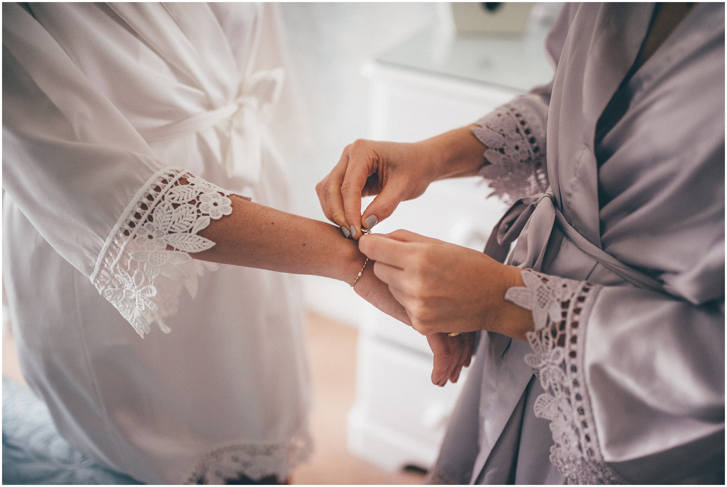 Bridesmaid fastens the bride's bracelet onto her wrist before the Cheshire wedding.